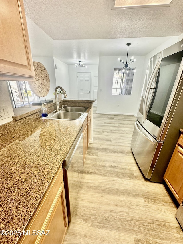 kitchen with light wood-type flooring, a sink, a textured ceiling, appliances with stainless steel finishes, and an inviting chandelier