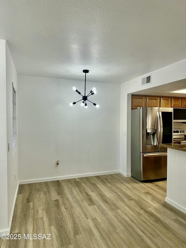 unfurnished living room featuring baseboards, visible vents, light wood finished floors, an inviting chandelier, and a textured ceiling