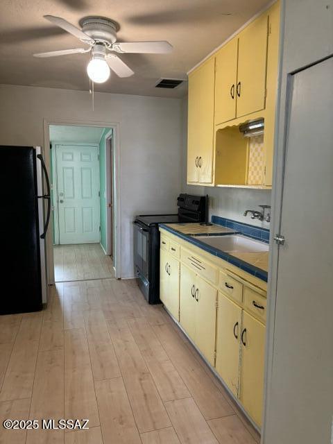 kitchen featuring light wood-type flooring, a ceiling fan, black electric range, a sink, and freestanding refrigerator