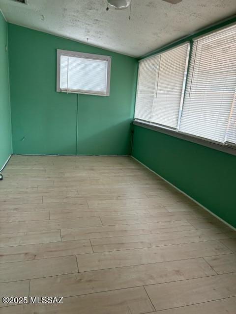 empty room featuring vaulted ceiling, visible vents, light wood finished floors, and a textured ceiling