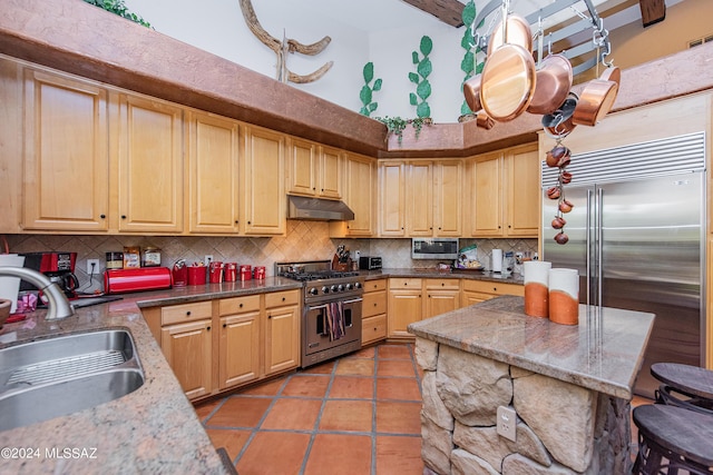 kitchen featuring high quality appliances, under cabinet range hood, a sink, light tile patterned floors, and decorative backsplash