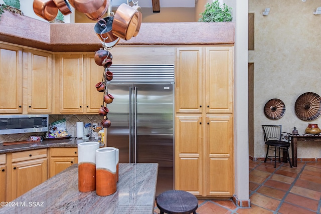 kitchen with tasteful backsplash, dark stone countertops, a high ceiling, tile patterned floors, and stainless steel appliances