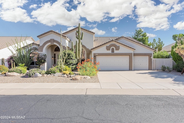 mediterranean / spanish-style home featuring fence, a tiled roof, stucco siding, driveway, and an attached garage