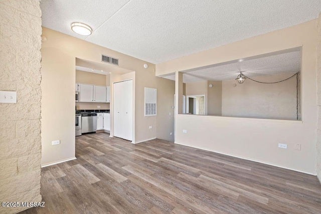 unfurnished living room with dark wood-type flooring, visible vents, and a textured ceiling