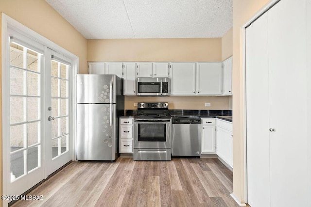 kitchen featuring a textured ceiling, dark countertops, appliances with stainless steel finishes, white cabinets, and light wood finished floors