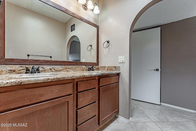 bathroom with a sink, baseboards, double vanity, and a textured wall