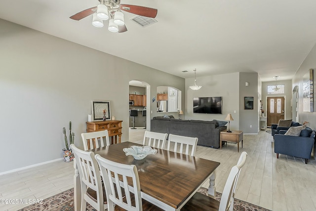 dining room with a ceiling fan, light wood-style flooring, baseboards, visible vents, and arched walkways