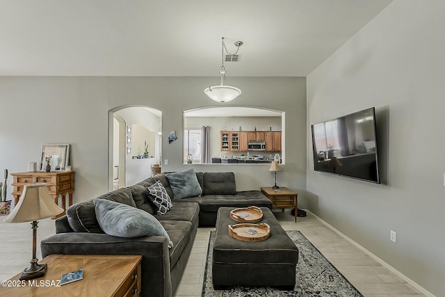 living area with arched walkways, baseboards, visible vents, and light wood finished floors