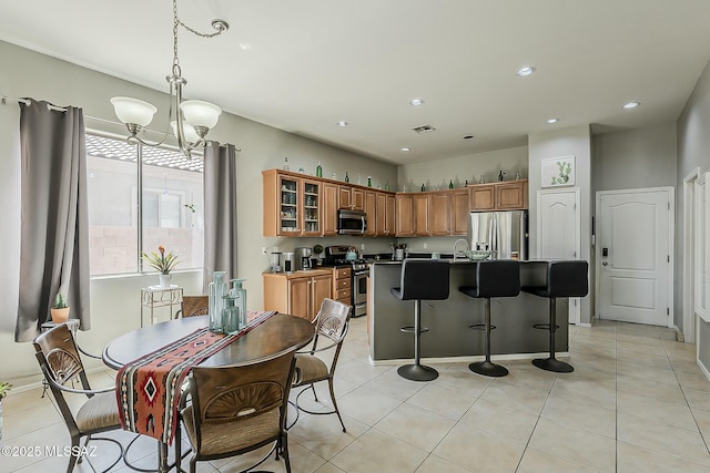kitchen featuring visible vents, brown cabinets, stainless steel appliances, glass insert cabinets, and a notable chandelier