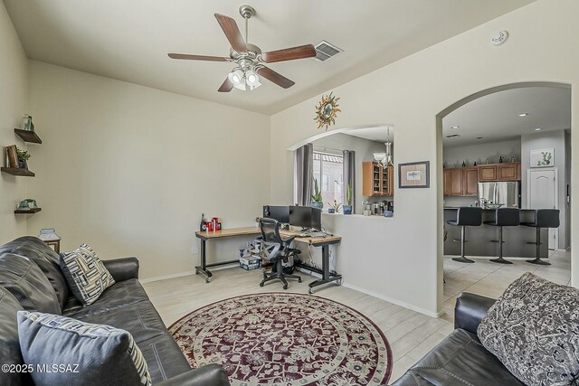 living room featuring light wood-type flooring, baseboards, visible vents, arched walkways, and ceiling fan