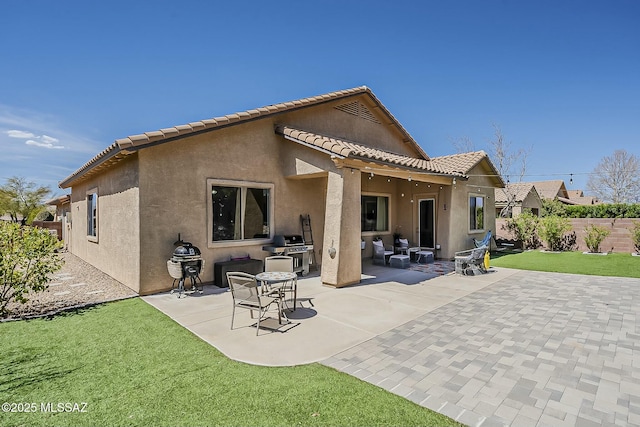 rear view of property featuring stucco siding, fence, a patio, a tiled roof, and a yard