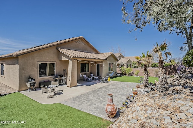 back of house featuring a tile roof, stucco siding, fence, a patio, and a lawn