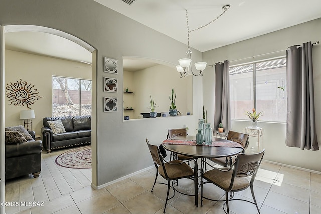 tiled dining room with arched walkways, baseboards, and vaulted ceiling
