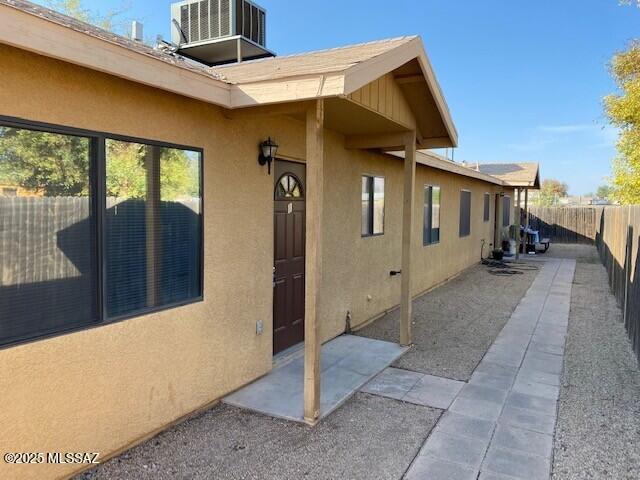 entrance to property with stucco siding, a patio, central AC unit, and fence