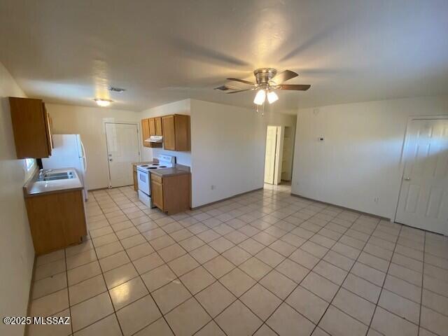 kitchen with light tile patterned floors, brown cabinets, white appliances, and a ceiling fan