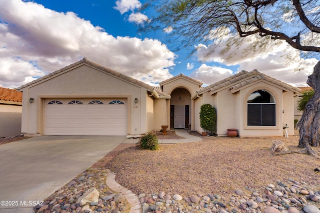 view of front facade featuring a tiled roof, a garage, driveway, and stucco siding