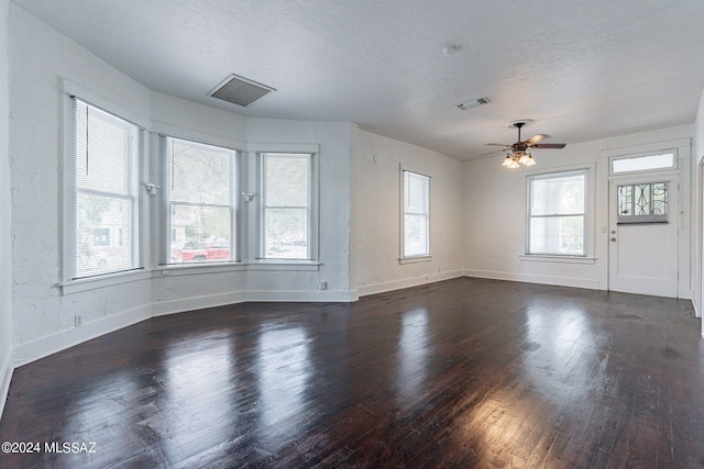 unfurnished living room featuring visible vents, baseboards, a textured ceiling, and dark wood finished floors