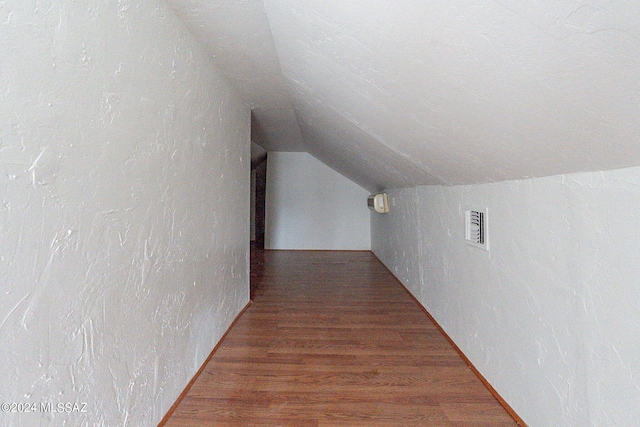 hall featuring lofted ceiling, wood finished floors, visible vents, and a textured wall