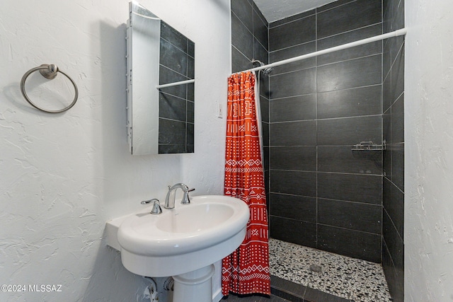 full bath with a tile shower, a sink, and a textured wall