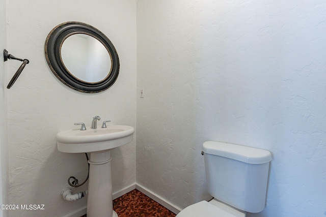 bathroom with toilet, a textured wall, and baseboards