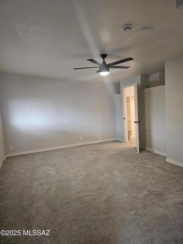 carpeted spare room featuring baseboards and a ceiling fan