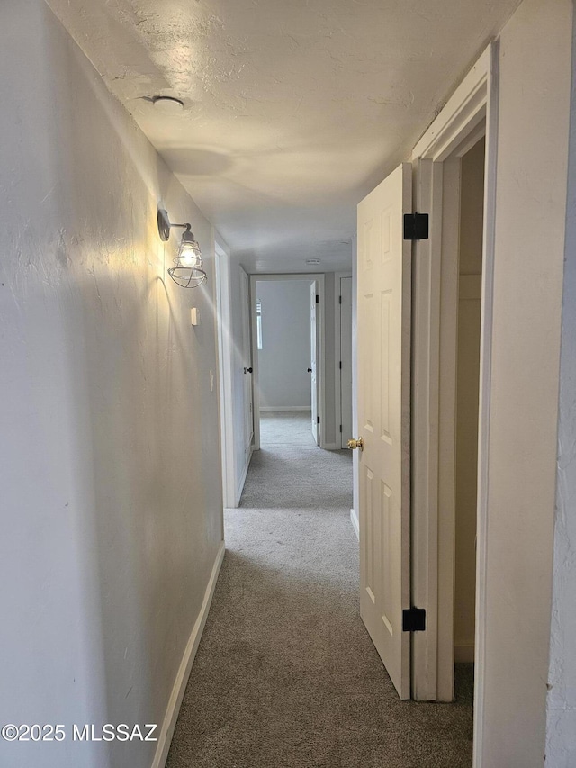 hall featuring baseboards and light colored carpet