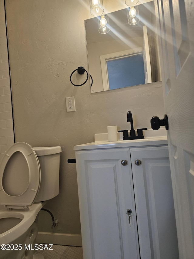 half bath featuring toilet, vanity, a textured wall, and baseboards