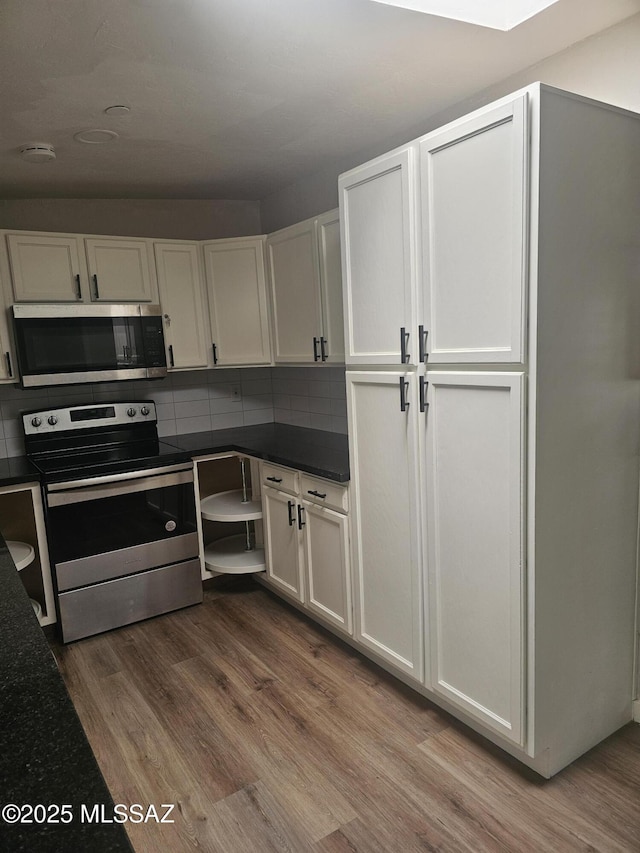 kitchen with white cabinets, wood finished floors, stainless steel appliances, dark countertops, and backsplash