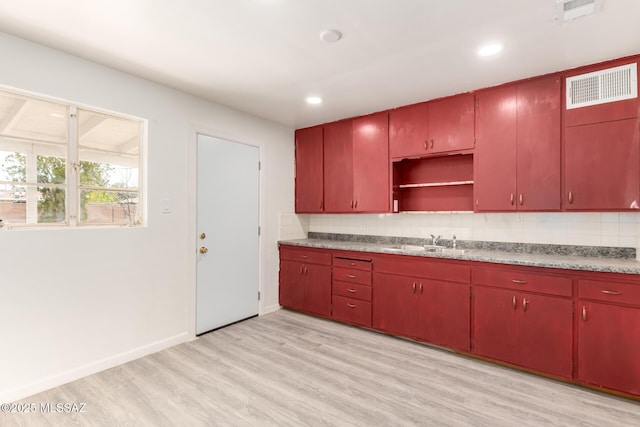 kitchen with tasteful backsplash, visible vents, red cabinetry, light wood-type flooring, and a sink