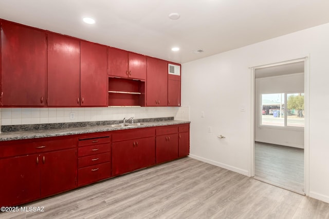 kitchen with red cabinetry, a sink, dark countertops, light wood-style floors, and decorative backsplash