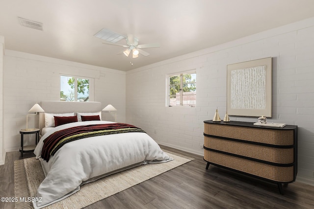 bedroom featuring visible vents, multiple windows, brick wall, and wood finished floors