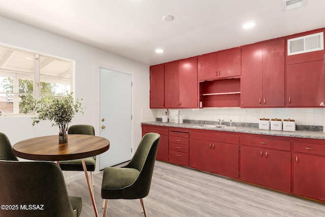 kitchen with red cabinetry, visible vents, tasteful backsplash, and a sink