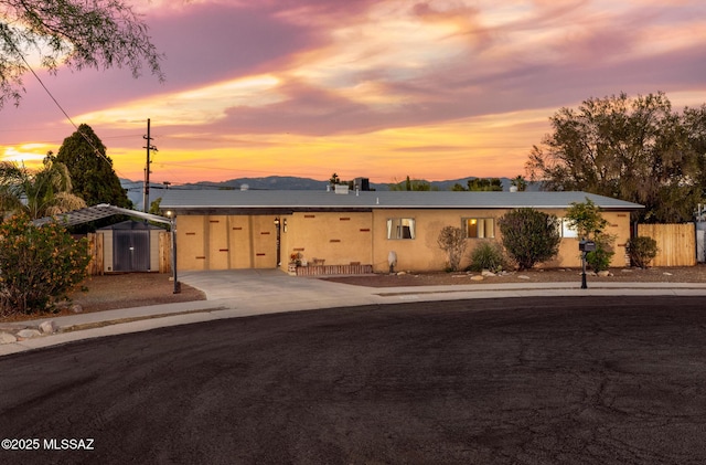 ranch-style house with a detached carport, fence, driveway, and stucco siding