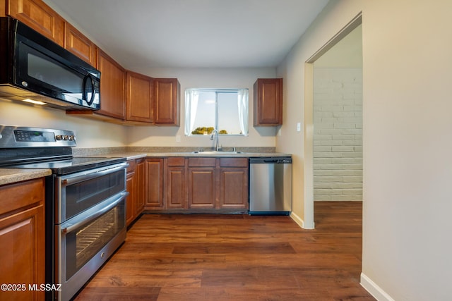 kitchen with appliances with stainless steel finishes, a sink, dark wood-style floors, and brown cabinetry