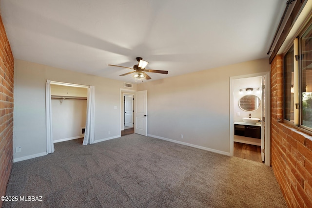 unfurnished bedroom with carpet floors, brick wall, ceiling fan, baseboards, and ensuite bath