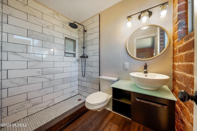 bathroom featuring a tile shower, wood finished floors, toilet, and vanity