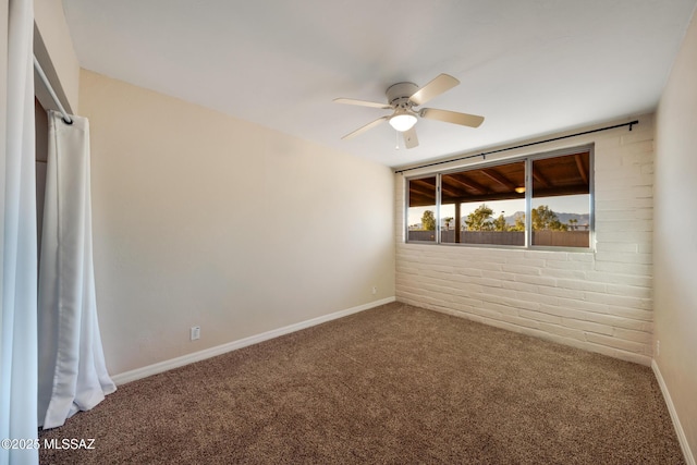 carpeted empty room featuring a ceiling fan, baseboards, and brick wall