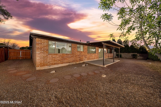 back of property at dusk featuring a patio area, brick siding, and fence