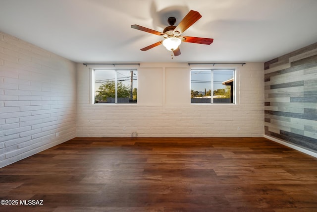 empty room featuring brick wall, ceiling fan, and dark wood-style floors