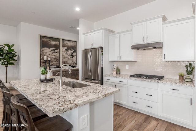 kitchen featuring light stone countertops, under cabinet range hood, decorative backsplash, appliances with stainless steel finishes, and a sink