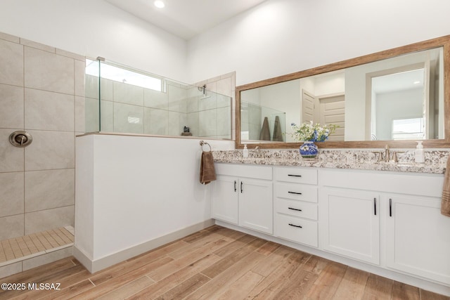 bathroom featuring double vanity, wood finished floors, a walk in shower, and a sink