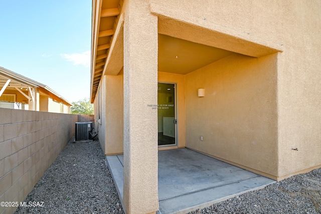 property entrance featuring central air condition unit, a patio area, fence, and stucco siding