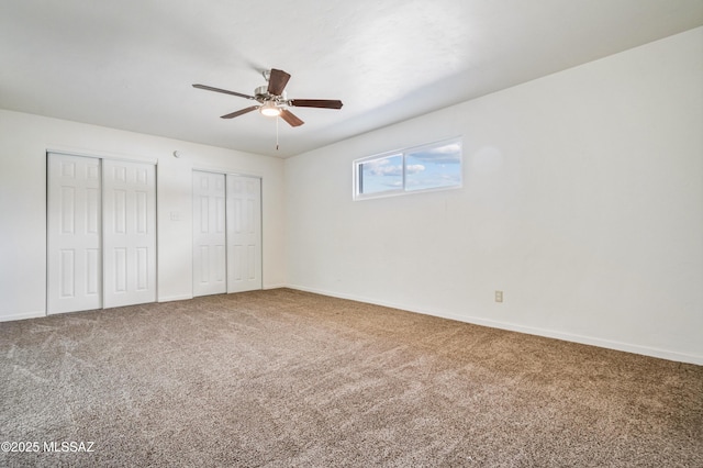 unfurnished bedroom featuring carpet flooring, baseboards, multiple closets, and ceiling fan