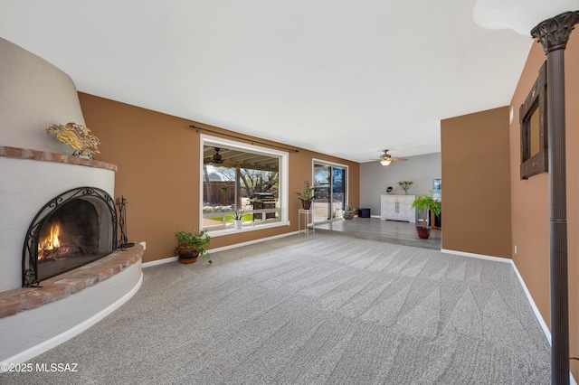 unfurnished living room with baseboards, carpet floors, a warm lit fireplace, and a ceiling fan