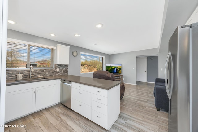 kitchen with dark countertops, open floor plan, appliances with stainless steel finishes, a peninsula, and a sink