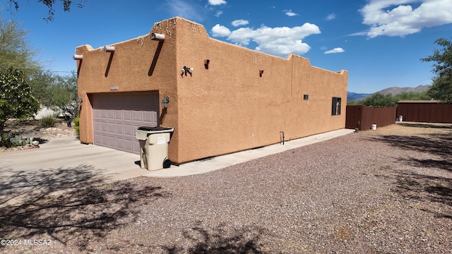 view of home's exterior featuring fence, concrete driveway, stucco siding, a garage, and a mountain view