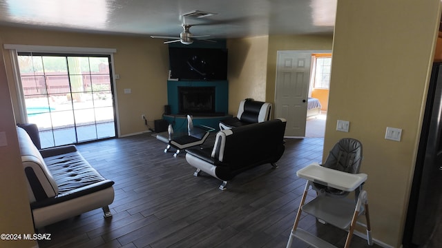 living room featuring visible vents, baseboards, a fireplace, dark wood-style floors, and a ceiling fan