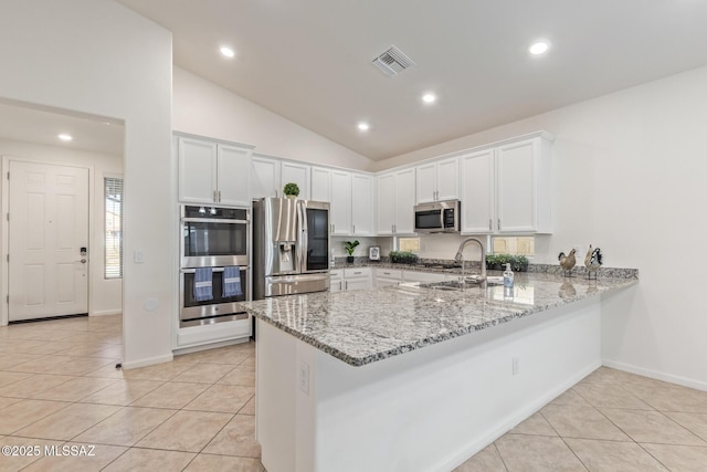 kitchen with a sink, a peninsula, light tile patterned flooring, and stainless steel appliances