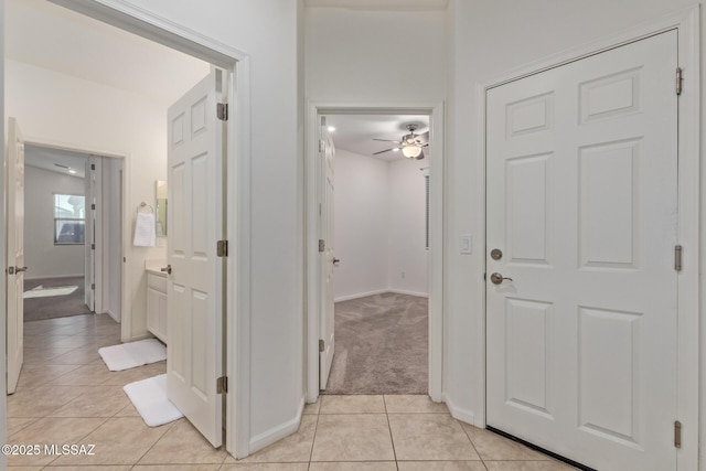 corridor with light tile patterned floors, baseboards, and light colored carpet