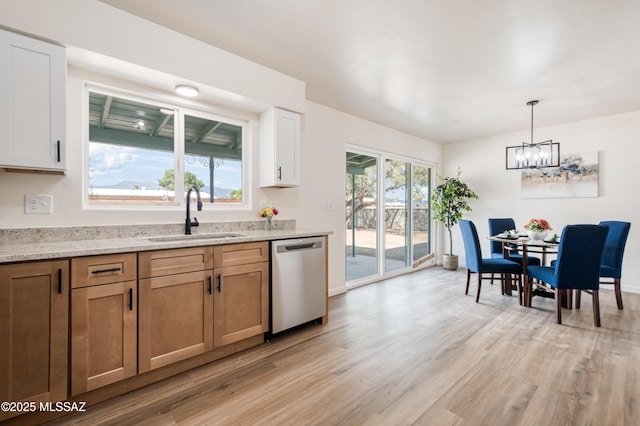 kitchen with light stone counters, an inviting chandelier, a sink, light wood-style floors, and dishwasher